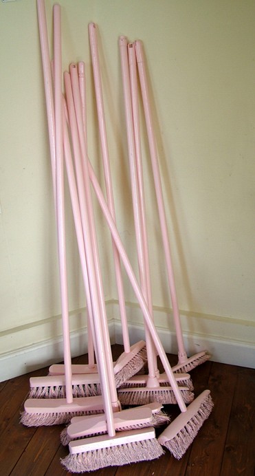 Installation « Les Balais roses » de Camille Fonteret : balais peints en rose, regroupés dans un angle de pièce (Gembloux, Belgique).