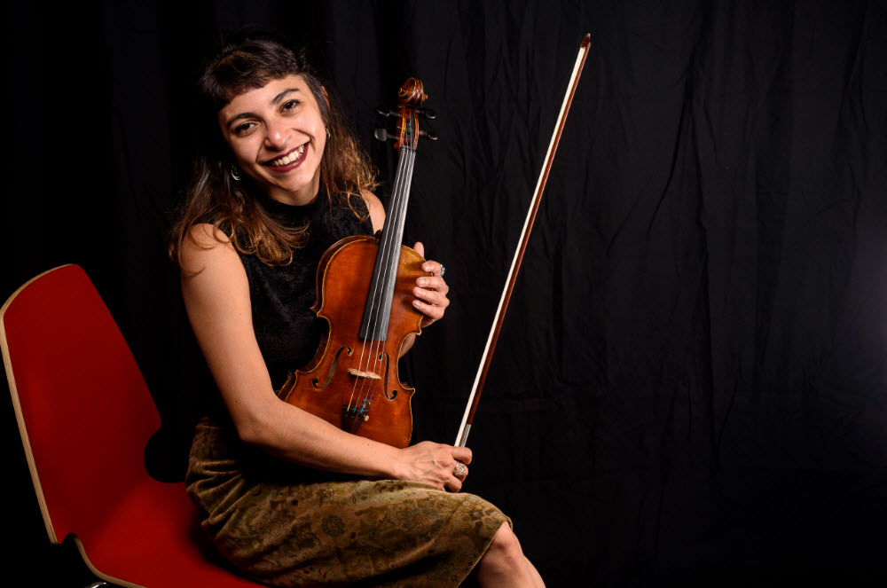 Portrait souriant d'Astrid Rios, violoniste professionnelle basée à Bruxelles, tenant son violon et son archet.